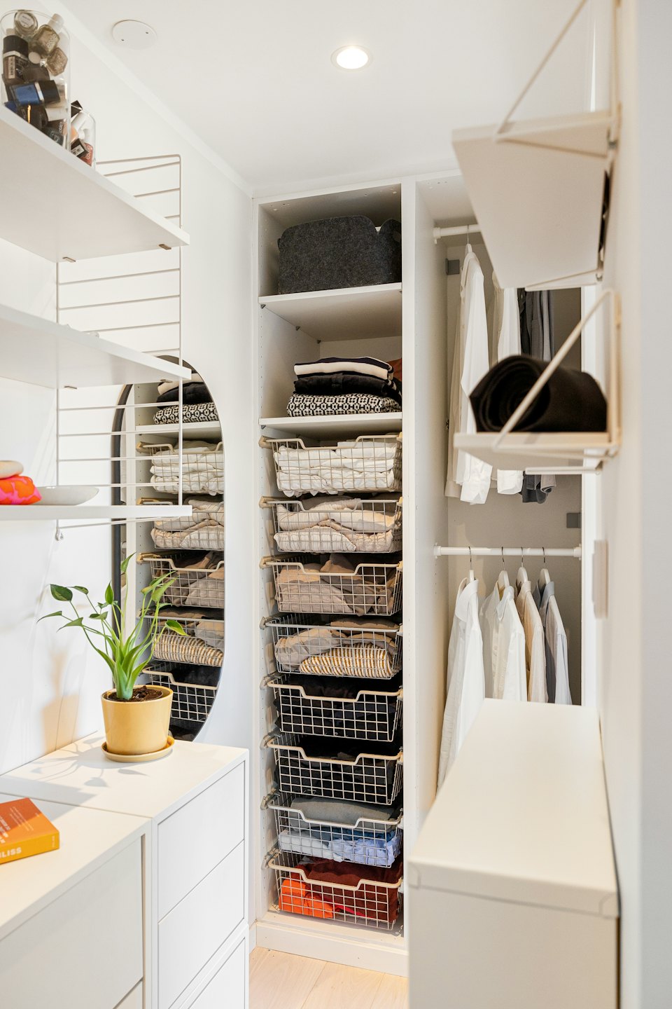 Organized white walk-in closet with folded clothes and hanging shirts.